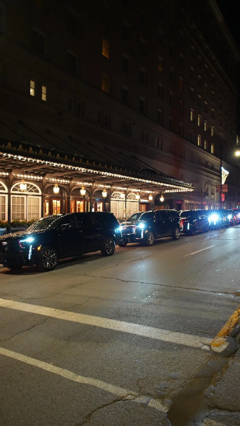 VUS noirs devant l’entrée illuminée du Ritz-Carlton, de nuit.